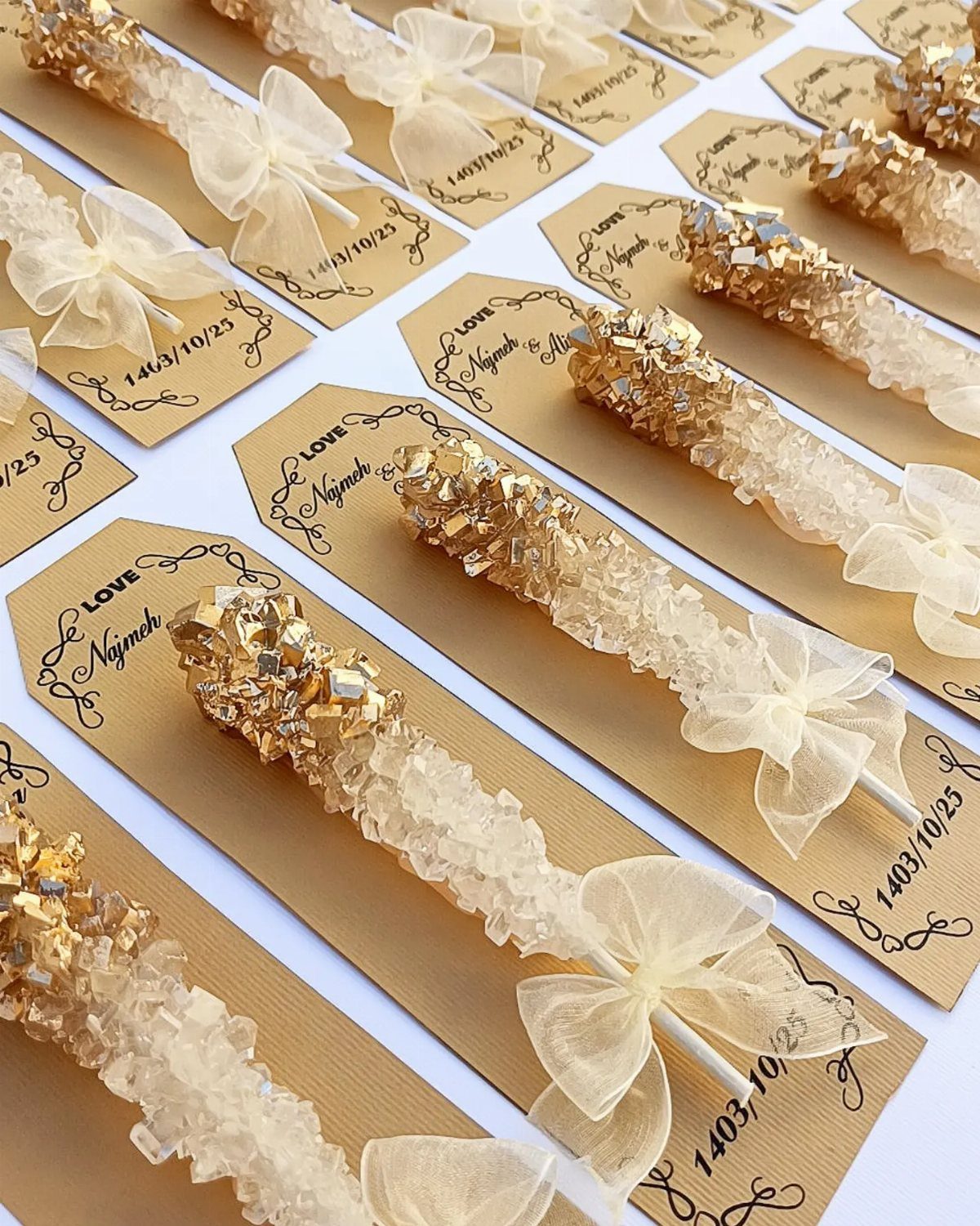 Gold and clear rock candy sticks with white bows on personalized brown tags.