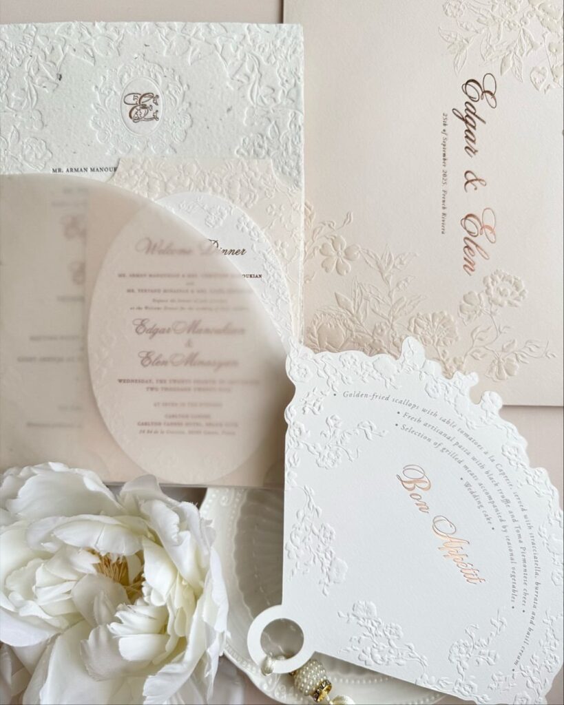 White embossed wedding invitations and stationery arranged with a white peony flower.