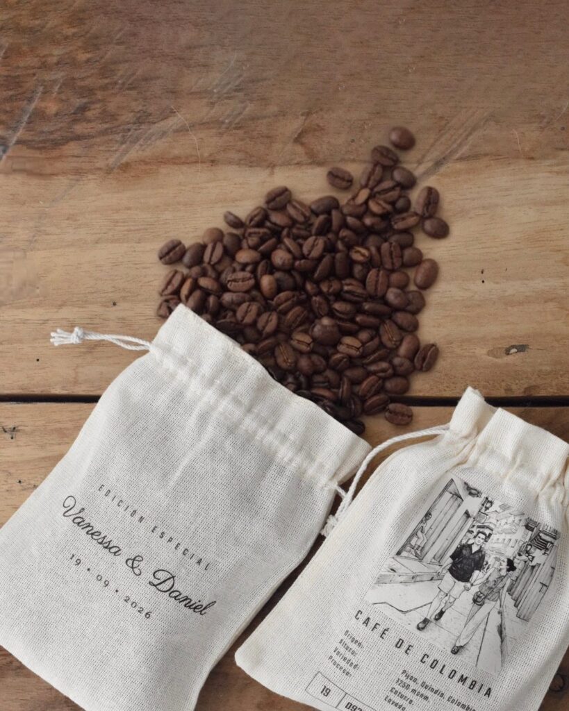 Two white fabric favor bags with names and coffee beans on wood.