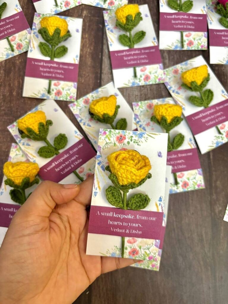Yellow crocheted roses attached to small white keepsake cards on a wooden table