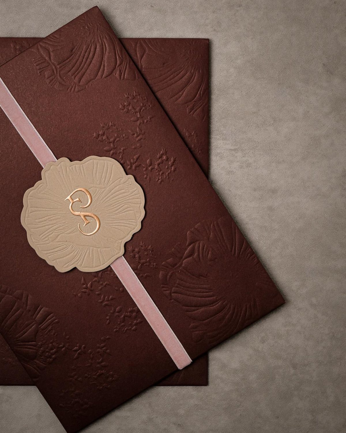 Dark brown embossed wedding invitations with a pink ribbon and gold wax seal.