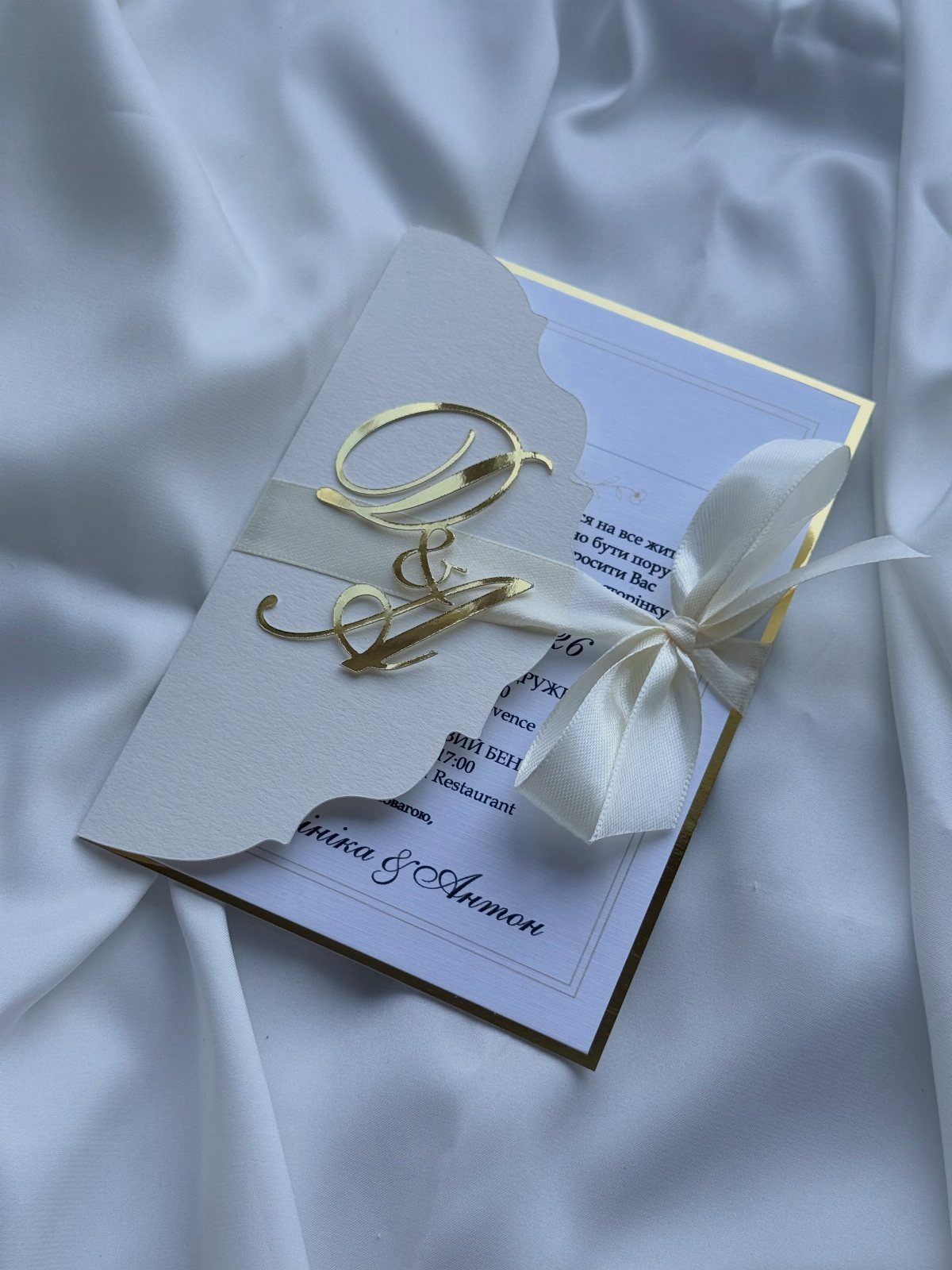 Formal wedding invitation with gold initials and white ribbon on satin fabric