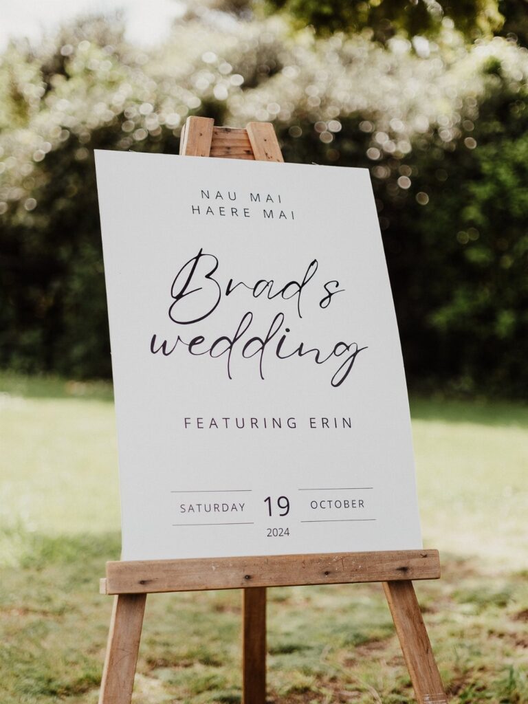 White wedding sign on a wooden easel reading Brad's wedding featuring Prin outdoors