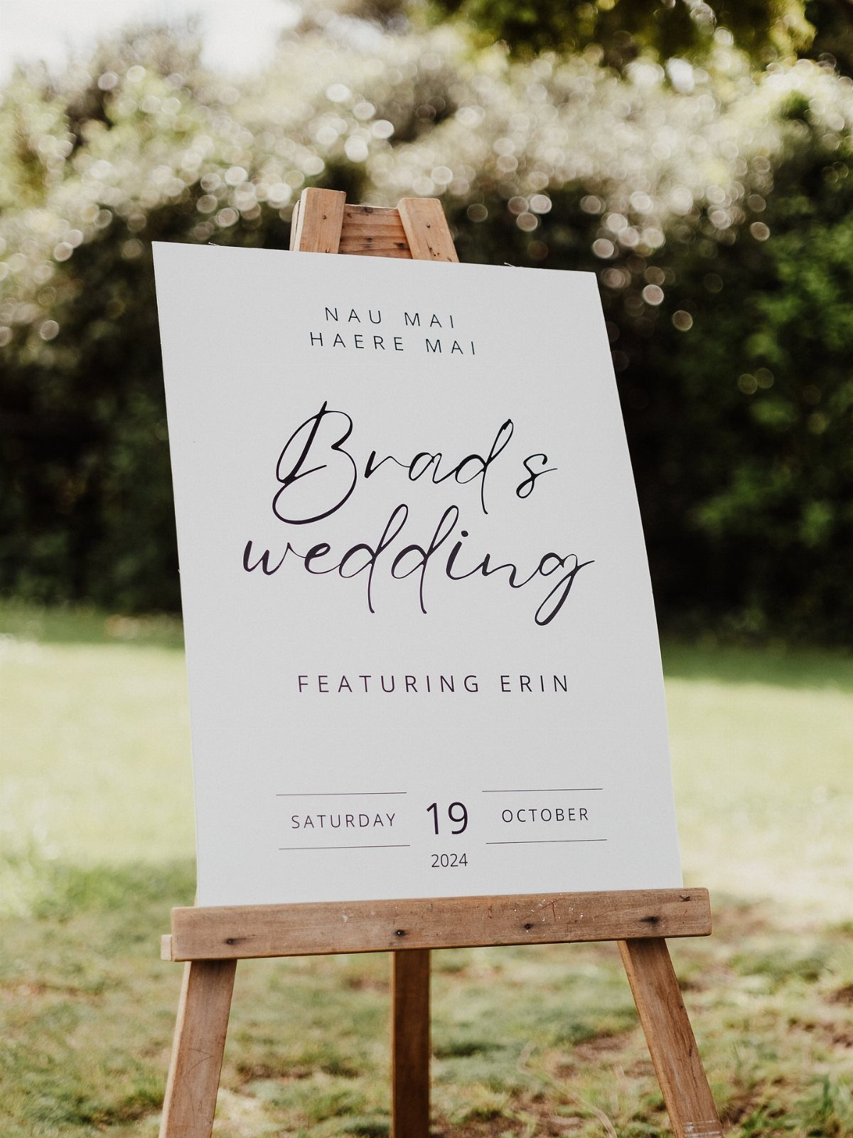 White wedding sign on a wooden easel reading Brad's wedding featuring Prin outdoors