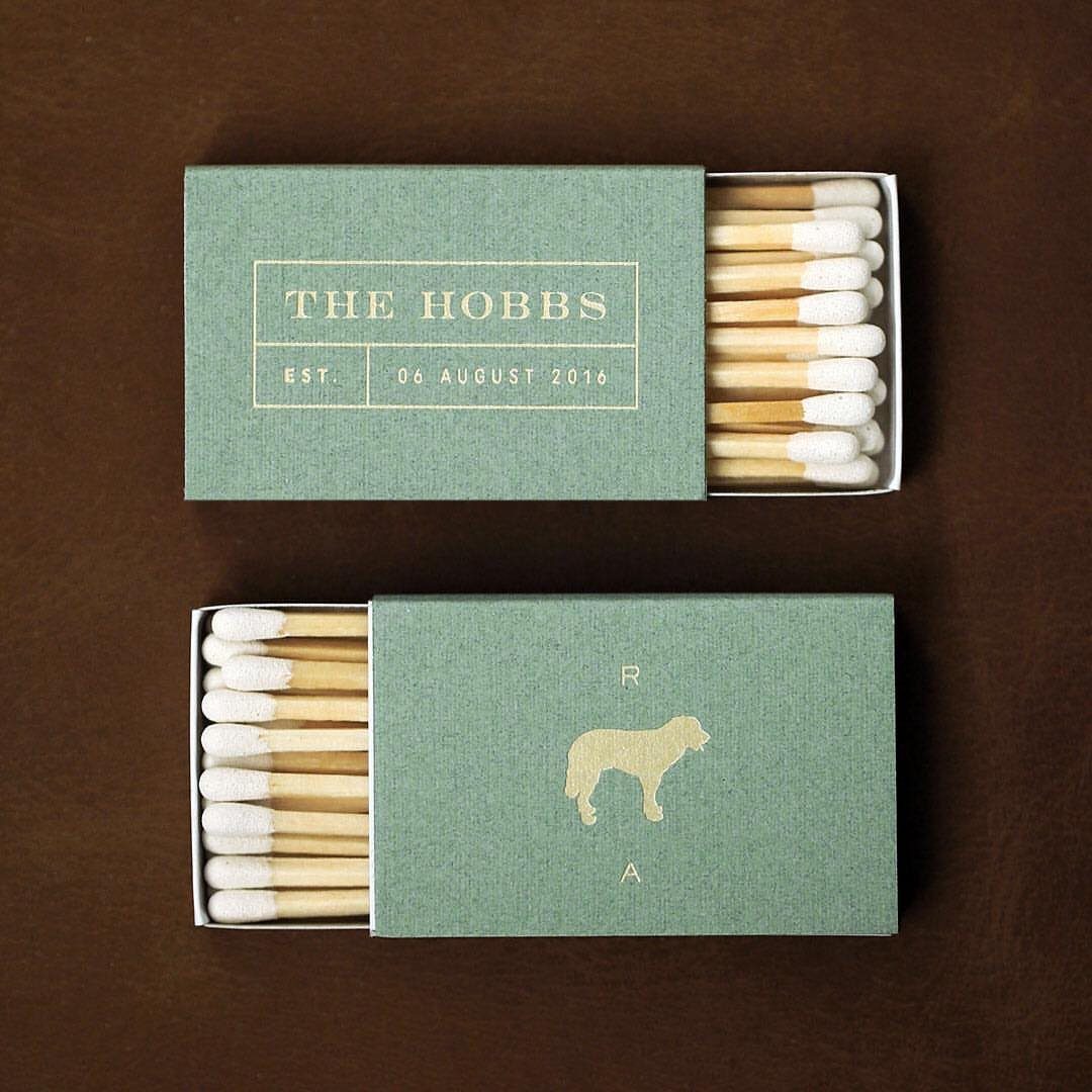 Sage green matchboxes with gold foil wedding text and a dog silhouette.