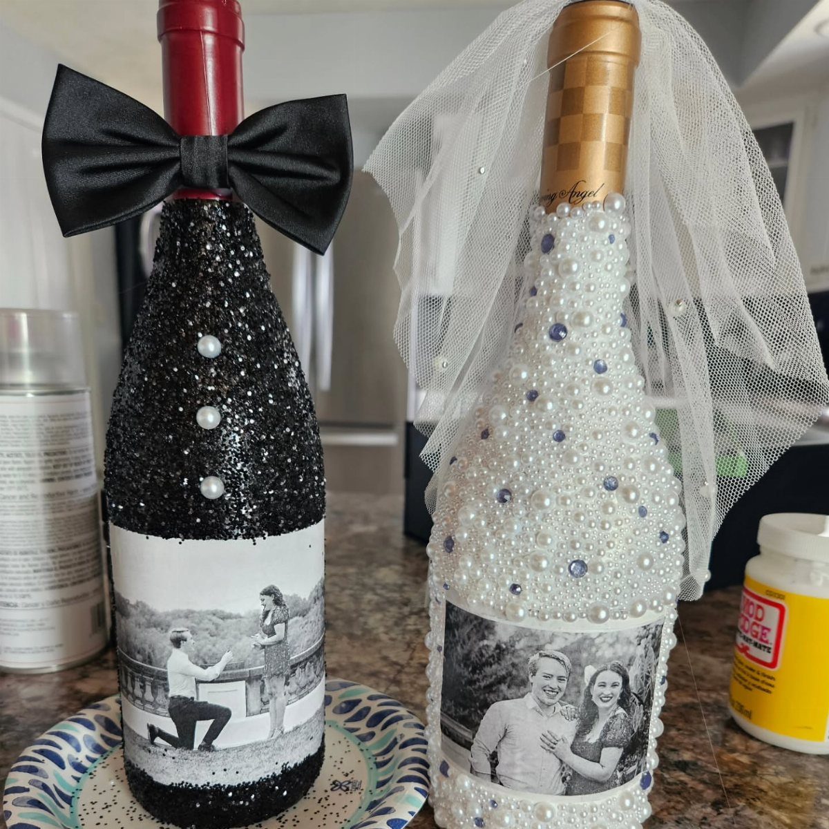 Two decorated wine bottles dressed as a bride and groom with photos and accessories.
