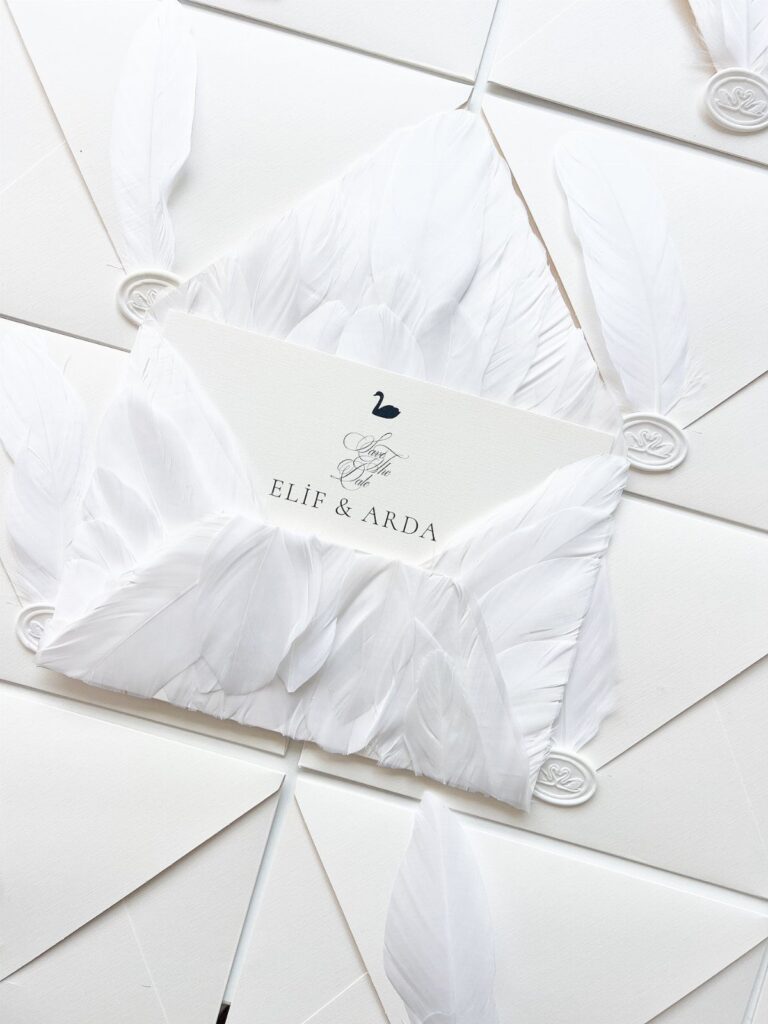 White wedding invitations with white feathers and wax seals on white envelopes.