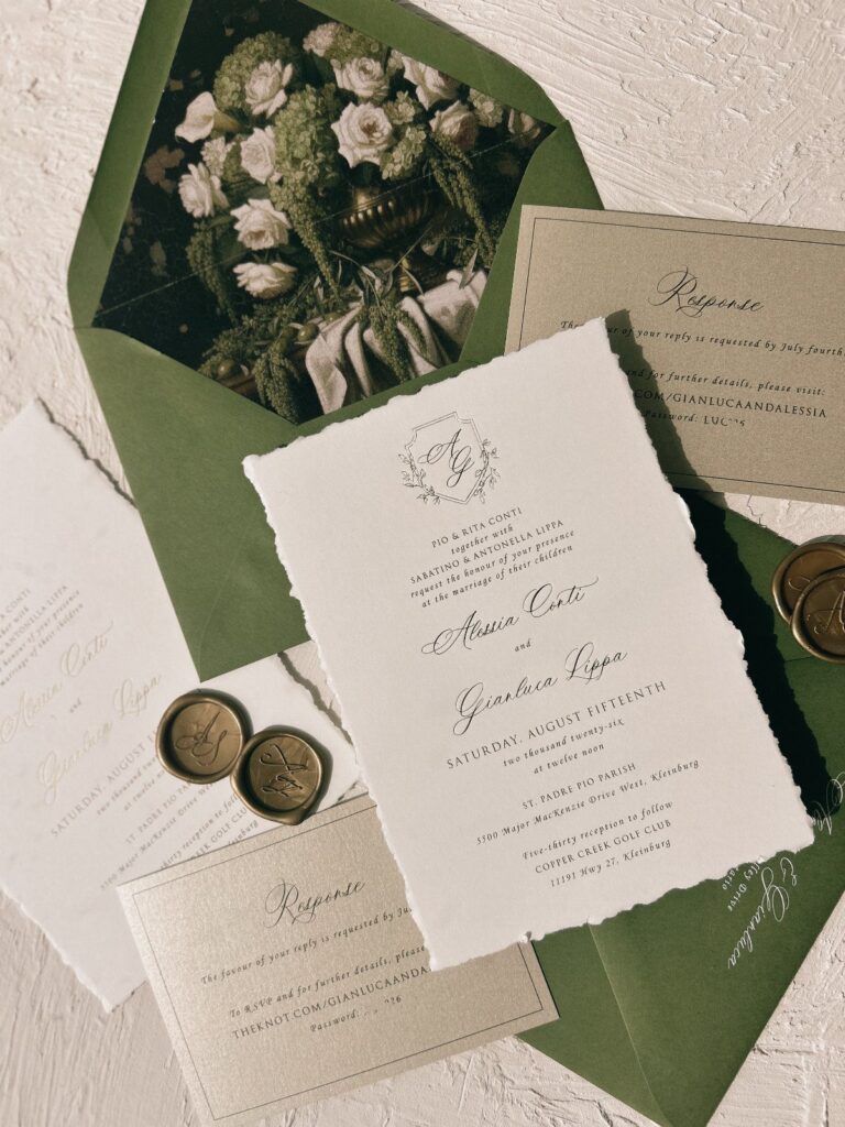 Wedding invitation suite with deckle-edged paper, green floral envelope, and gold wax seals.