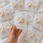 Pearl flower and gold ring ornaments packaged as wedding favors on white cards.