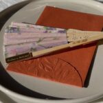 Floral folding fan on a terracotta napkin and white plate as a wedding favor