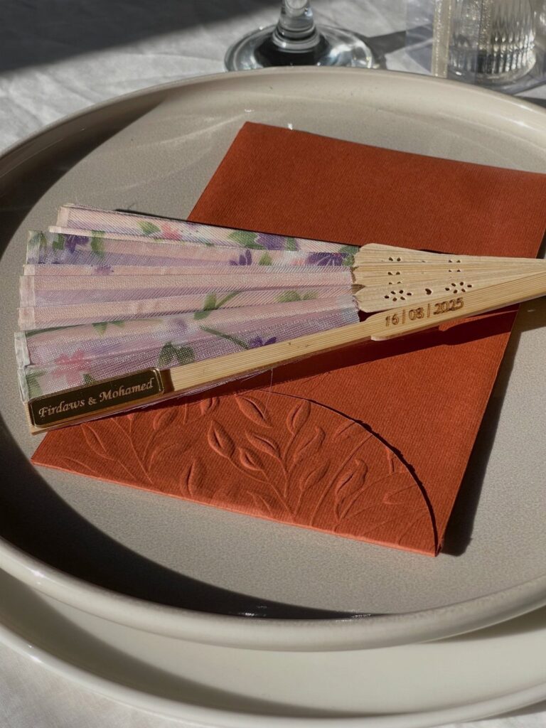 Floral folding fan on a terracotta napkin and white plate as a wedding favor