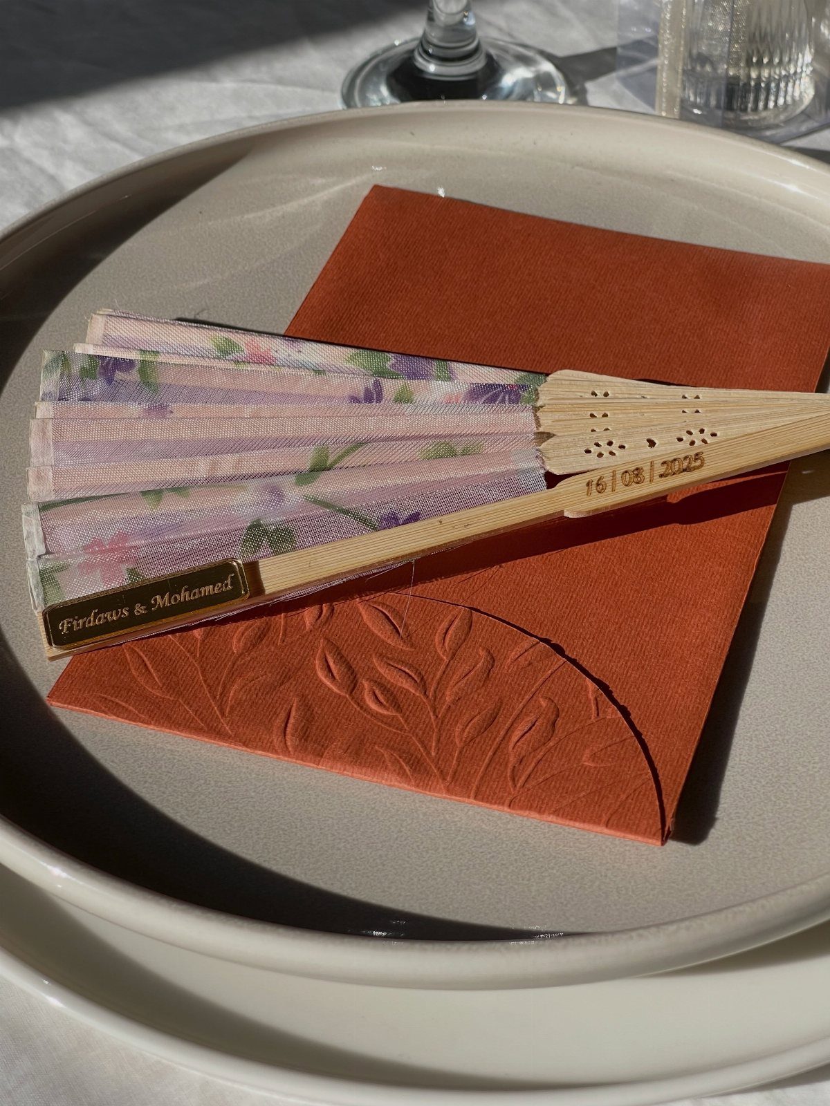 Floral folding fan on a terracotta napkin and white plate as a wedding favor