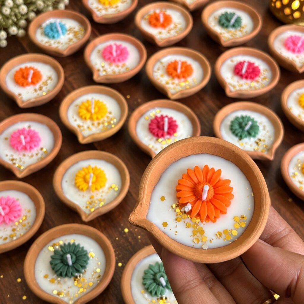 Terracotta diyas filled with white wax and colorful flower-shaped candles and gold glitter.