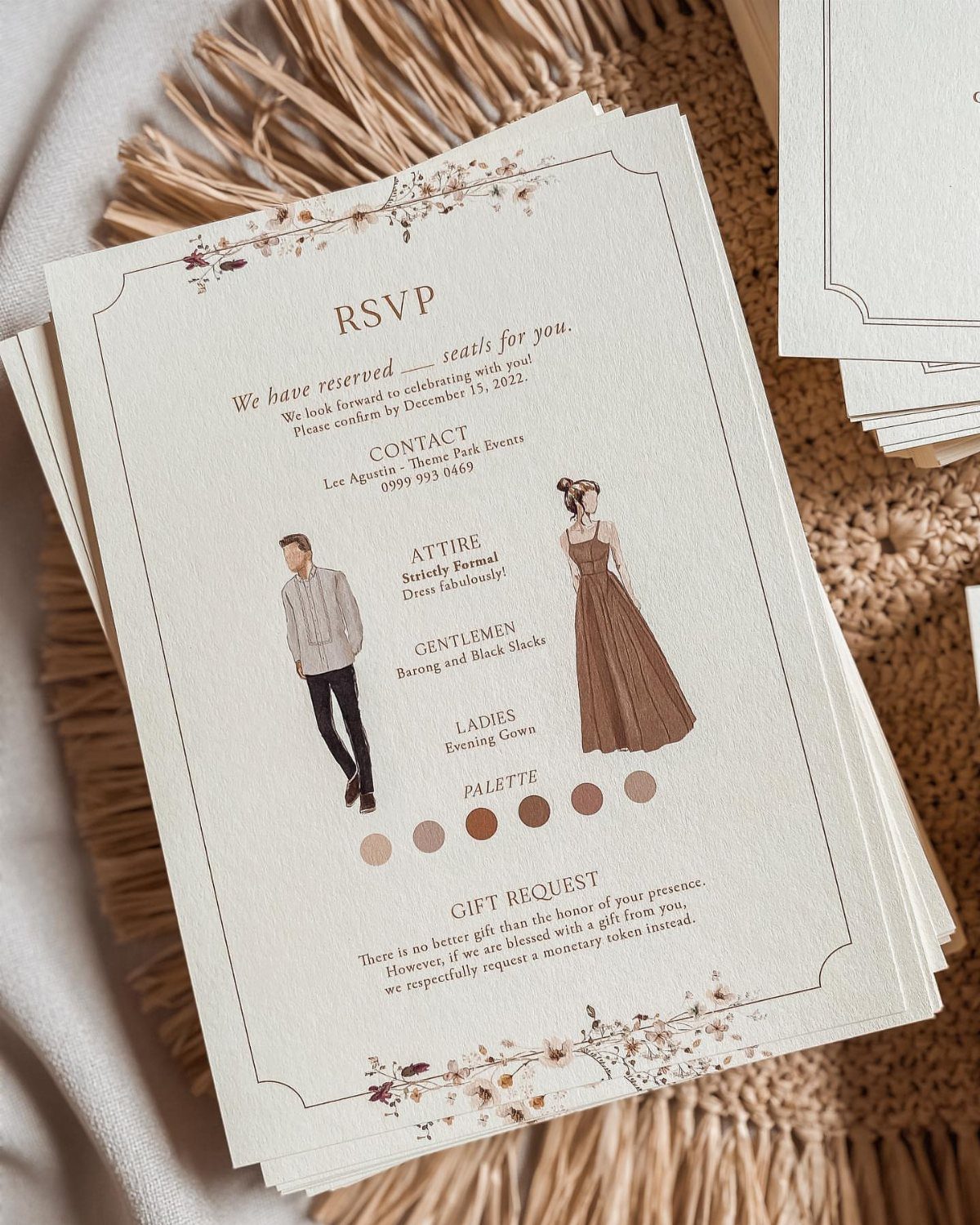 Cream RSVP cards with floral accents and attire illustrations on a woven mat.