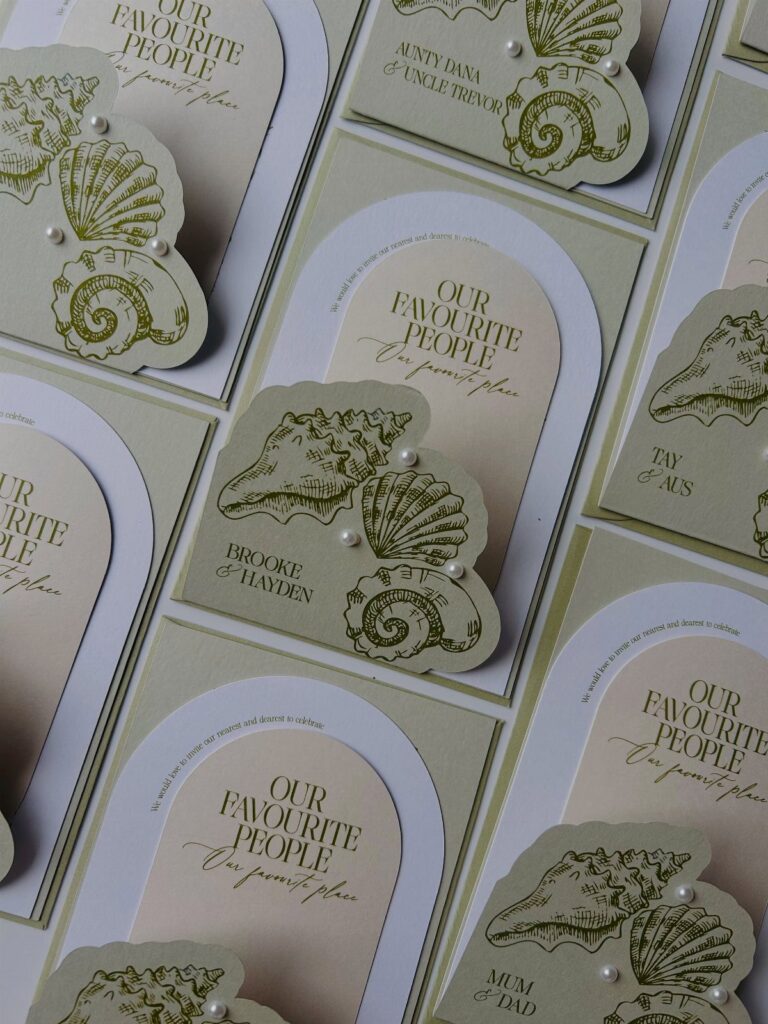 Wedding invitations with olive green seashell cutouts and pearl accents on cream paper.