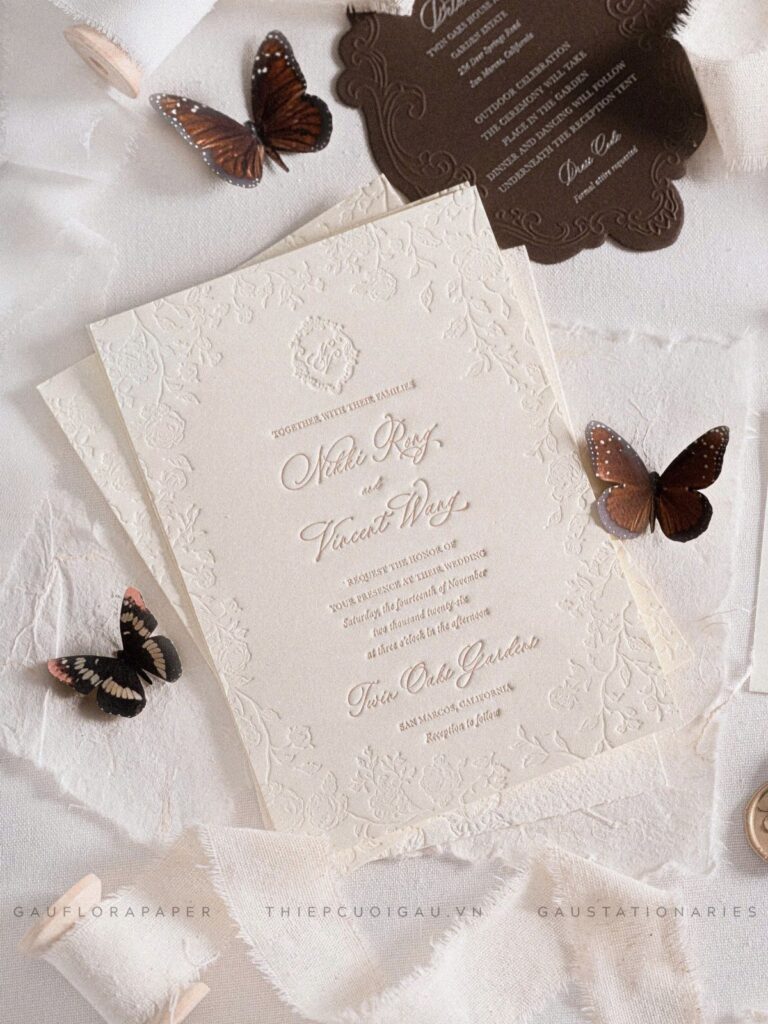 Embossed cream wedding invitations with brown butterflies on white textured fabric.