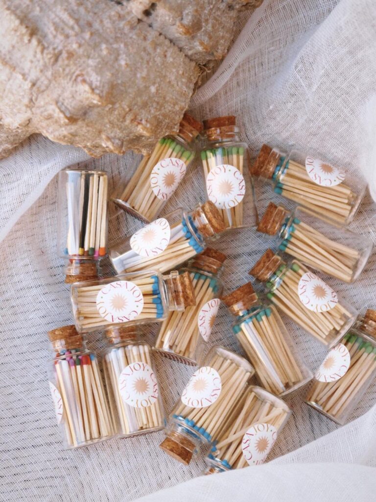 Small glass vials filled with wooden matches and floral labels on white fabric.