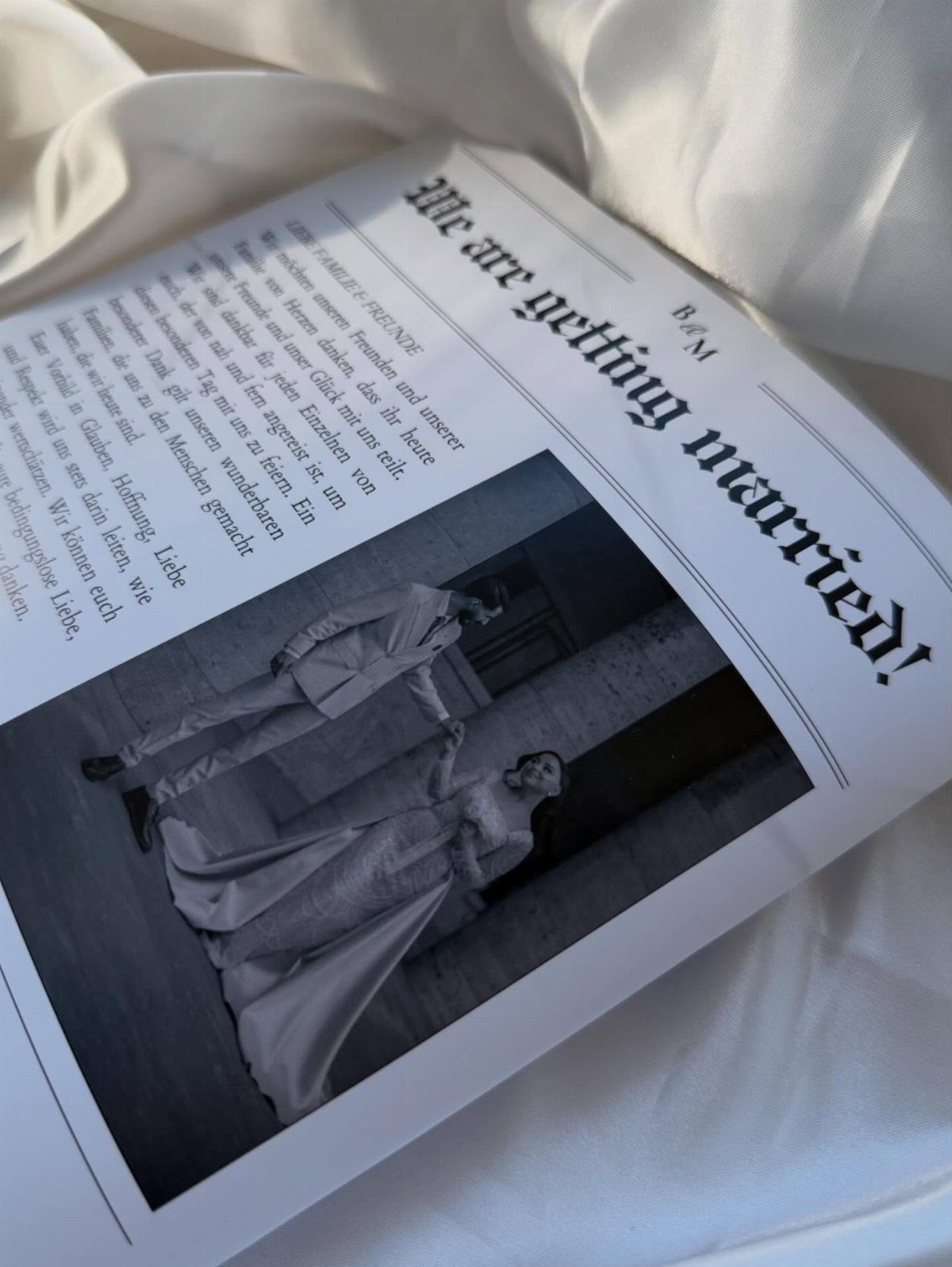Wedding newspaper invitation with a black and white couple photo on white fabric.