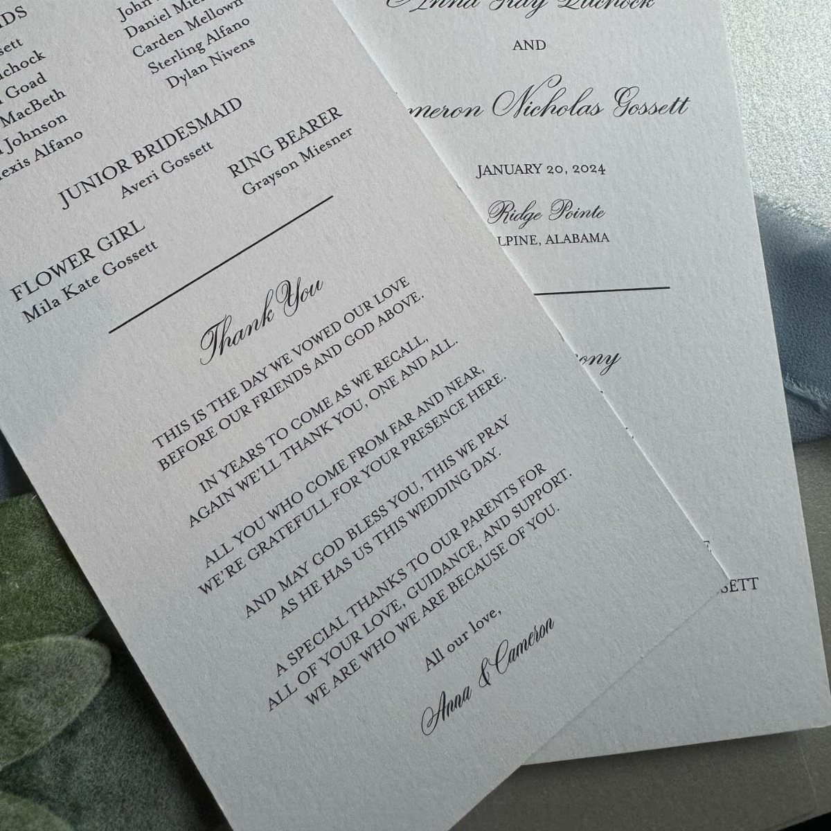 White textured wedding program cards with elegant black text and a grey leaf.