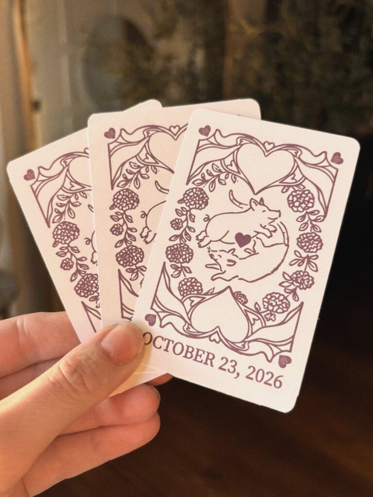 Custom playing cards with maroon pig illustrations and a wedding date held by hand.