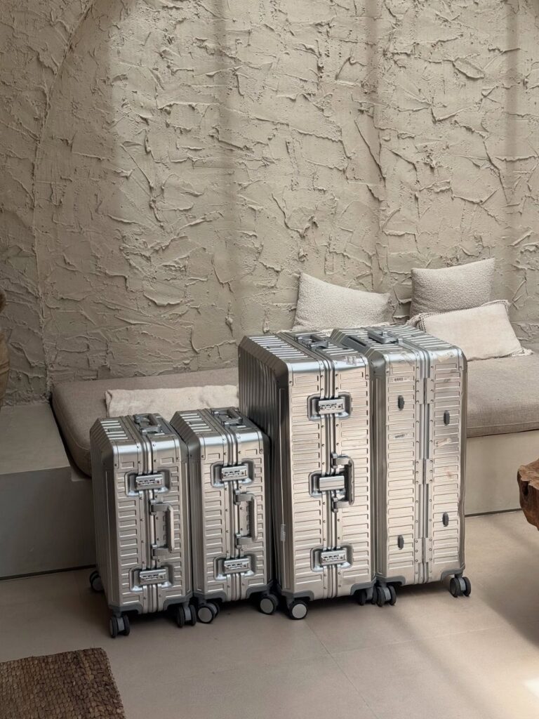 Three silver aluminum suitcases of different sizes standing in a neutral-toned room.