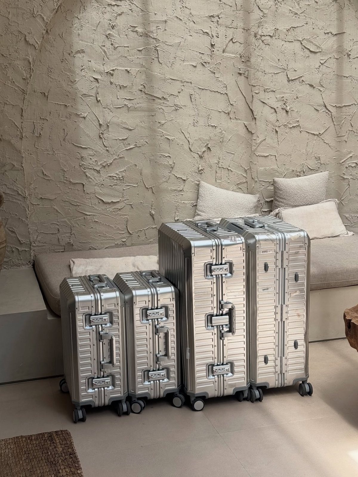 Three silver aluminum suitcases of different sizes standing in a neutral-toned room.