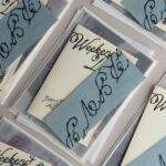 Wedding invitation sets with cream cards, blue-grey bands, and translucent vellum envelopes.