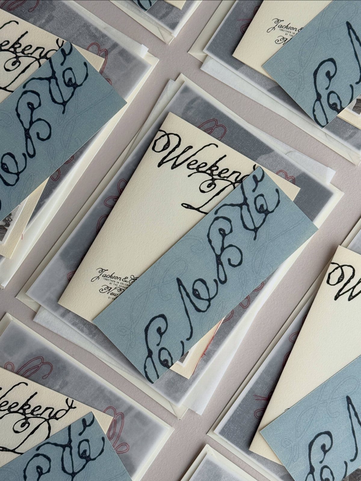 Wedding invitation sets with cream cards, blue-grey bands, and translucent vellum envelopes.