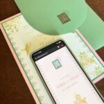 Smartphone showing a wedding website next to matching physical invitations and green envelope