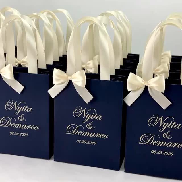 Navy blue wedding welcome bags with white satin bows and gold personalized text.